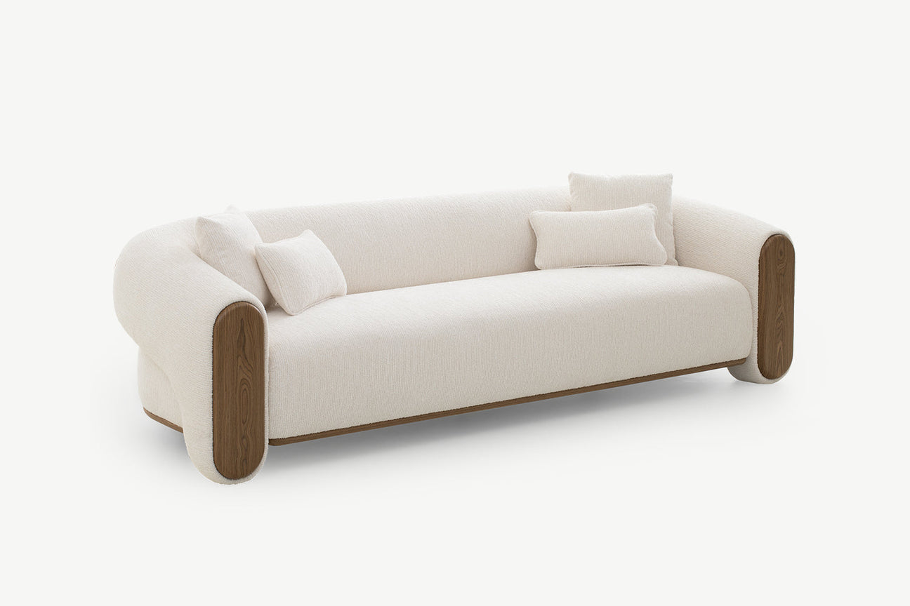 Modern curved cream fabric sofa with wooden armrests and three cushions on a clean white background.