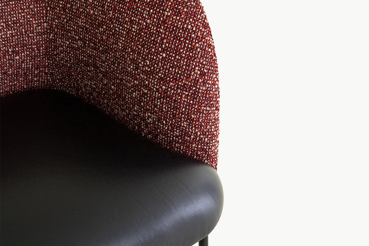 Angled perspective of the Angela Armchair, displaying its distinctive curved bouclé back, compact leather seat, and attached minimalist side table
