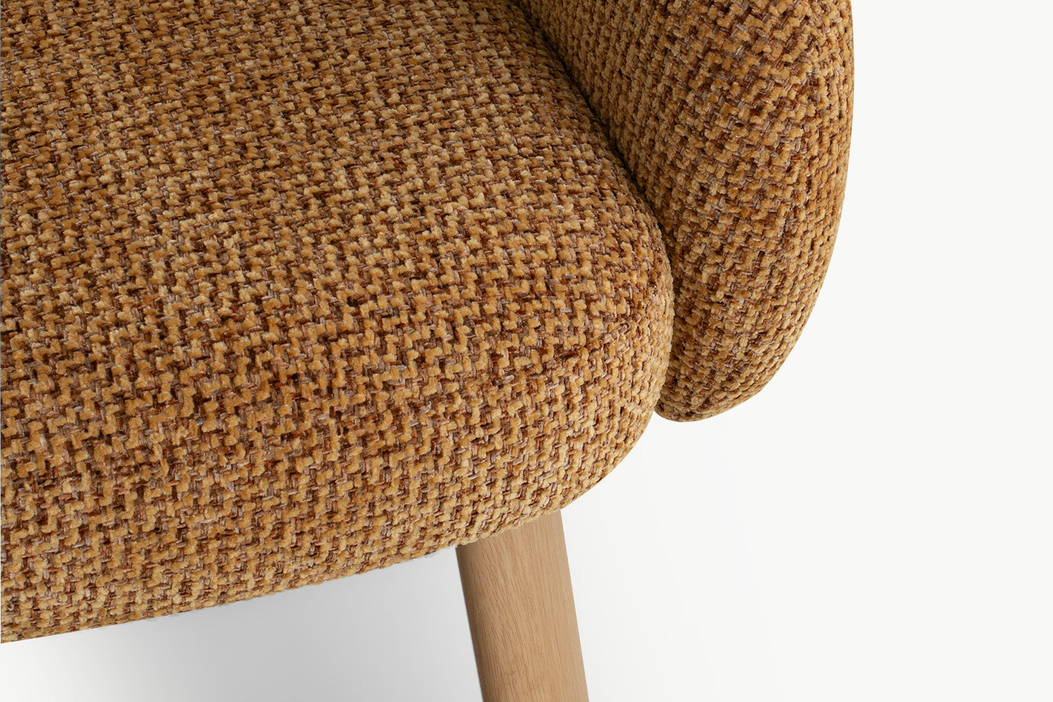 Foto close-up resolusi tinggi kain bouclé lembut warna cokelat karamel hangat, sandaran tangan melengkung ergonomis, dan kaki kayu oak muda model tapered pada kursi aksen yang stylish.