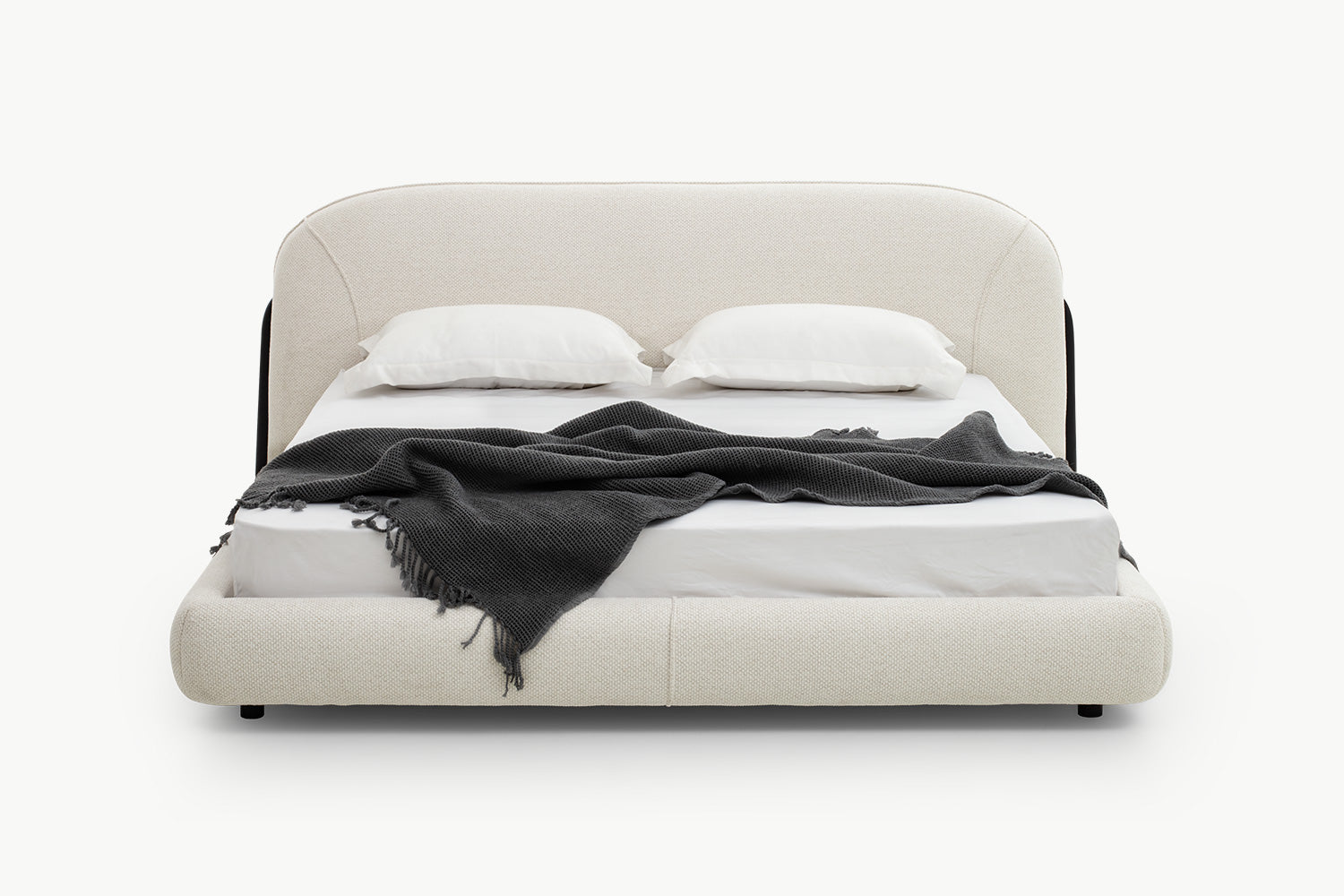 Modern upholstered bed with curved beige fabric headboard, padded low-profile frame, and sleek black legs for a contemporary bedroom centerpiece