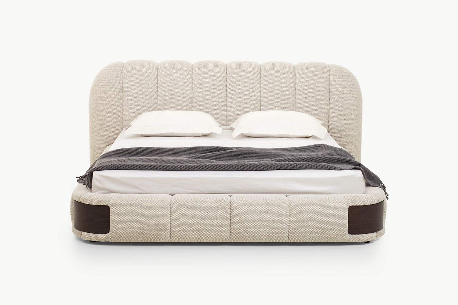 Luxurious upholstered bed with tall scalloped channel-tufted headboard in soft beige textured fabric and padded segmented base with dark wood side accents