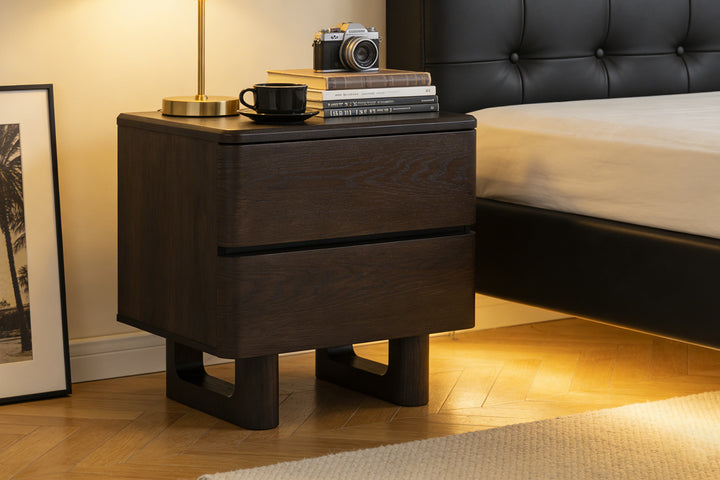 Nakas Chris kayu oak gelap yang elegan di samping tempat tidur, ditata dengan lampu kuningan, kamera, buku, dan secangkir kopi hangat—gaya kamar tidur modern