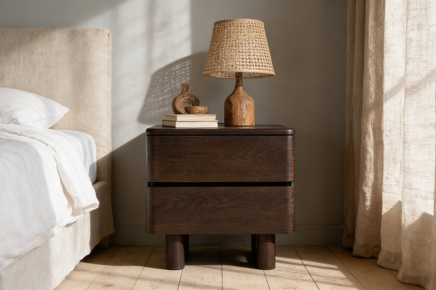 Nakas Chris kayu oak gelap ditata dengan lampu meja rotan, dekorasi kayu natural, mangkuk kecil, dan buku—gaya kamar tidur minimalis yang hangat