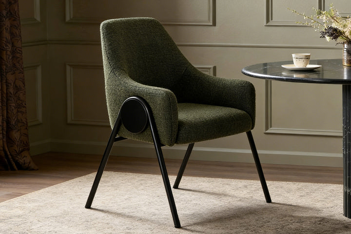 High-quality dining chair in rich olive green boucle upholstery positioned beside a marble-top table in a sophisticated dining space with neutral walls and soft lighting, blending comfort with refined aesthetics.