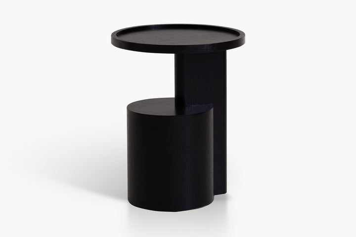 Modern round black side table with tall cylindrical pedestal and integrated lower shelf, featuring matte textured finish and clean minimalist lines